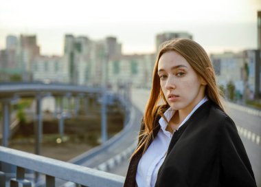 Şehrin arka planında köprüde poz veren beyaz bir genç kız. Üzgün kadın kameraya bakıyor..