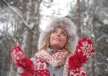 Forest Park 'taki sarışın kadın portresi. Kürk kürk şapkalı, kırmızı eldivenli, beyaz eşarplı güzel bir kız. Kış modası. Mavi gözler. Arka planda karlı ağaçlar var. Yukarı bakıyorum.