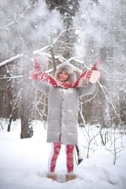 Sarışın kadın tatilde. Havaya kar atıyor. Gülen surat. Tatlı kız kırmızı atkı, örgü eldivenler, gri kürk şapka ve şık bir ceket giyiyor. Hava güzel ve kar yağıyor. Tam boy kadın.