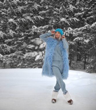 Karlı ormanda güzel bir kızın kış portresi. Sarışın kadın kış parkında yürüyor. Mavi şapkalı bayan..  