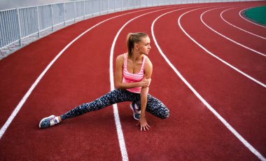 Bacağını esneten kaslı sarışın kadın. Spor. Kaçak. Stadyumda koşmadan önce esneyen sporcu kadın.