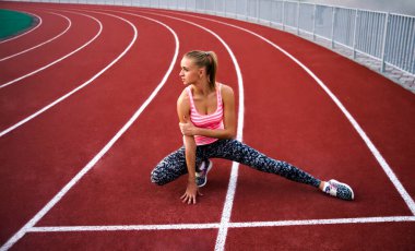 Bacağını esneten kaslı sarışın kadın. Spor. Kaçak. Stadyumda koşmadan önce esneyen sporcu kadın.