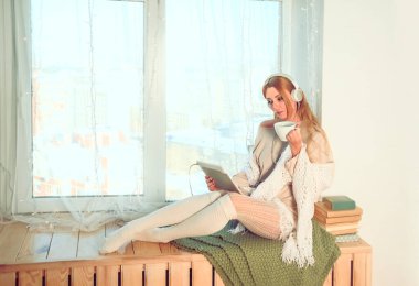 Kadın pencere eşiğinde oturuyor ve e-kitap okuyor.. 