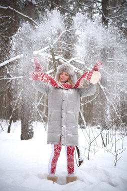 Sarışın kadın tatilde. Havaya kar atıyor. Gülen surat. Tatlı kız kırmızı atkı, örgü eldivenler, gri kürk şapka ve şık bir ceket giyiyor. Hava güzel ve kar yağıyor. Tam boy kadın.