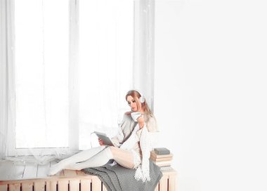 Kadın pencere eşiğinde oturuyor ve e-kitap okuyor.. 