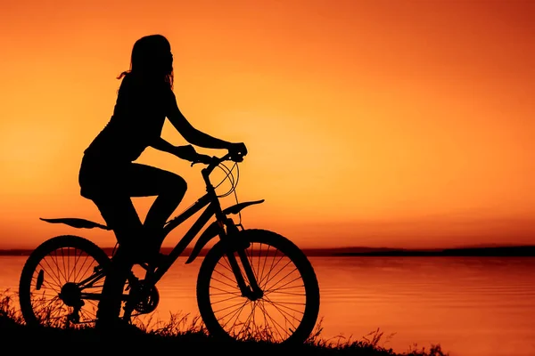 シルエットの女性が自転車に乗っています 日没の海の背景 — ストック写真
