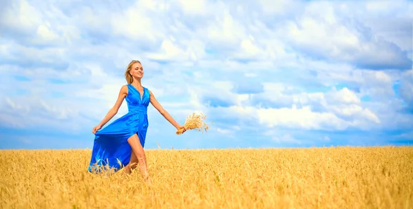 小麦の畑を駆け抜けるロマンチックなスリムな女性 鮮やかなブルーのロングドレスを着た女性 可愛い若い大人の女の子は青空に向かって歩く 夏の日 — ストック写真