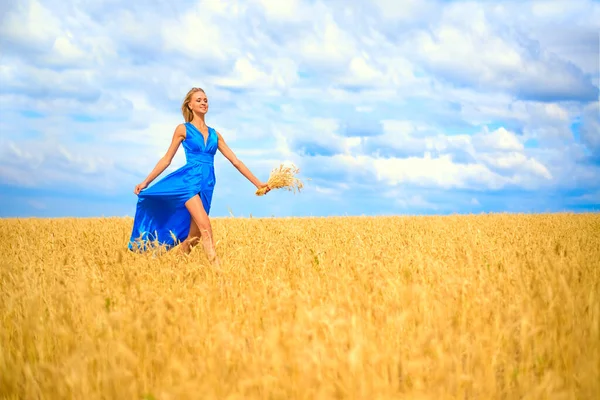 小麦の畑を駆け抜けるロマンチックなスリムな女性 鮮やかなブルーのロングドレスを着た女性 可愛い若い大人の女の子は青空に向かって歩く 夏の日 — ストック写真