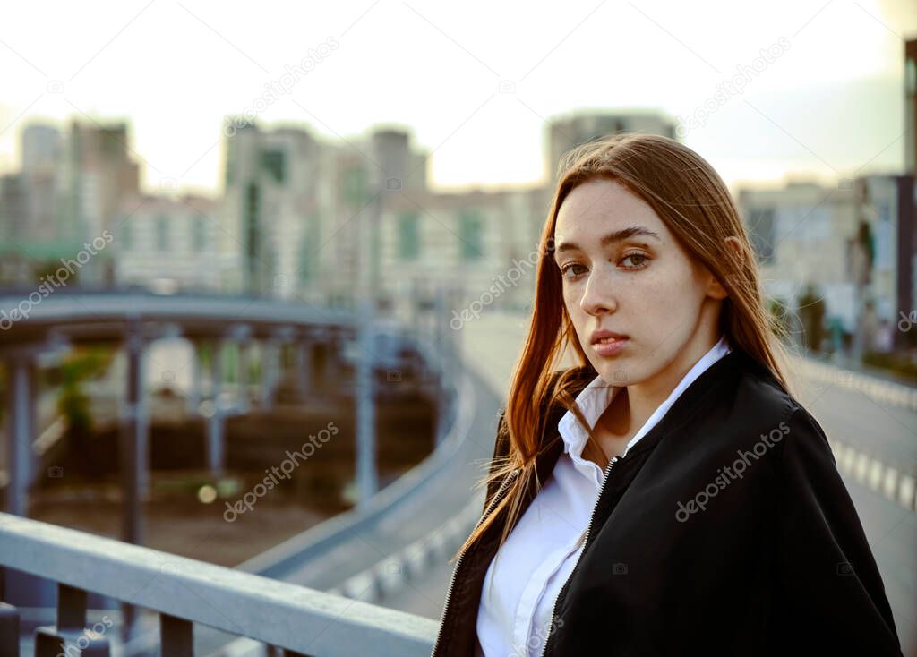young caucasian girl posing on bridge on city background. sad woman looking at camera.