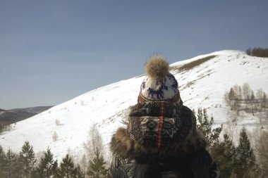 Örgü şapka ve ceket giyen kız. Dağ zemininde duran kadın. Arka plan