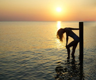 Deniz kıyısında duran bir kadın silueti. Güneş ışığı. Kız güneşli günbatımının tadını çıkarıyor. Sarı uzun saçlı..