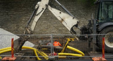Bir kazıcı ve iki kazıcı halka açık bir yolda drenaj borusu açmak için bir çukur kazıyor. Yeraltı kıvrımlı boru döşeme