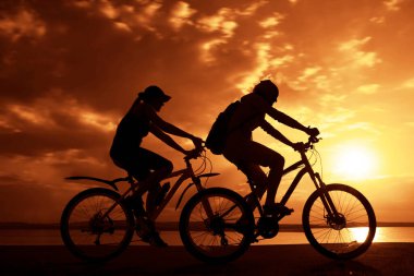Boşluk. Gün batımında bisiklete binen sportif arkadaşlar. Bisikletçiler sahil boyunca gidiyor. Doğa arka planında spor.