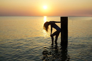 Deniz kıyısında duran bir kadın silueti. Güneş ışığı. Kız güneşli günbatımının tadını çıkarıyor. Sarı uzun saçlı..