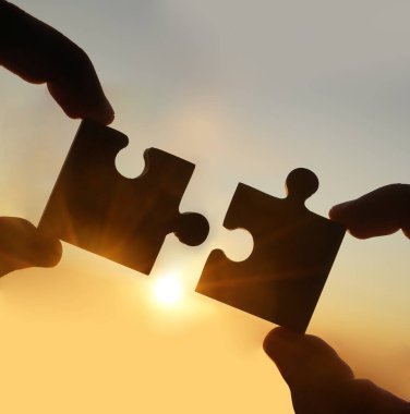 Gökyüzü arka planında yapboz parçaları olan eller.  