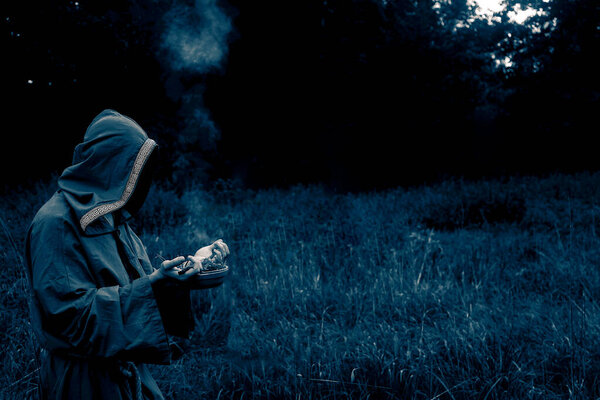 shaman with a censer inflates incense. man wear green shroud against evening forest. 