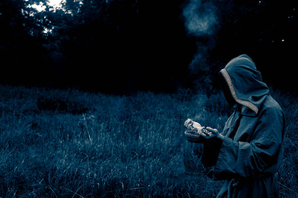 shaman with a censer inflates incense. man wear green shroud against evening forest. 