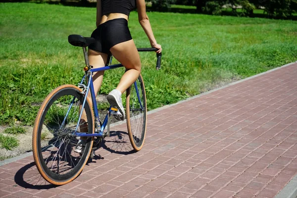 woman cyclist on  hipster bike.  Back view. no face. paving slabs in summer park.