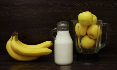 Ayakta duran süt şişesi ve taze muzların yanında sarı elmalarla dolu bir blender. Smoothie için malzemeler