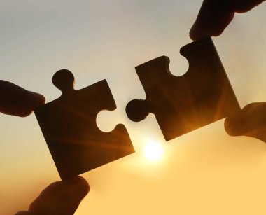 Gökyüzü arka planında yapboz parçaları olan eller.  