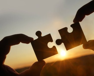 Gökyüzü arka planında yapboz parçaları olan eller.  