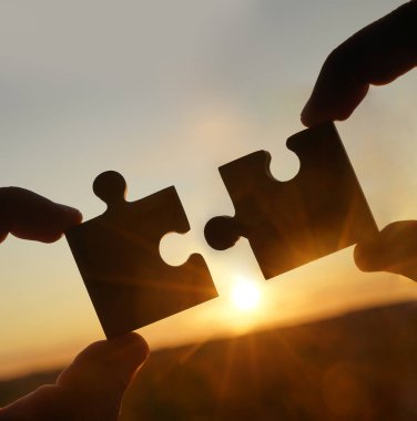 Gökyüzü arka planında yapboz parçaları olan eller.  