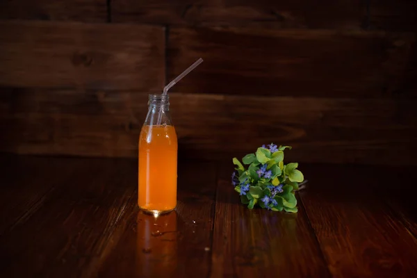 Botella vintage con jugo, paja y flores en la mesa de madera — Foto de Stock