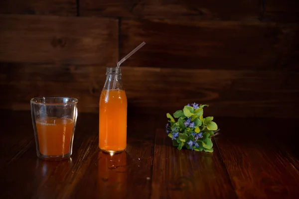 Garrafa vintage com suco, palha e flores na mesa de madeira — Fotografia de Stock