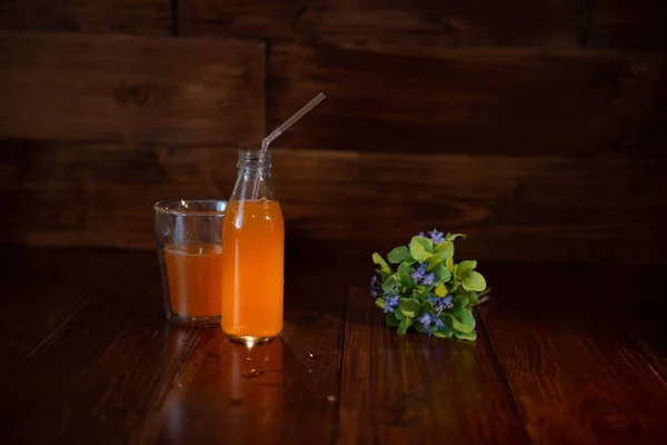 Botella vintage con jugo, paja y flores en la mesa de madera — Foto de Stock