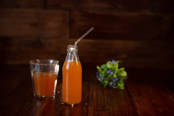 Weinflasche mit Saft, Stroh und Blumen auf Holztisch — Stockfoto