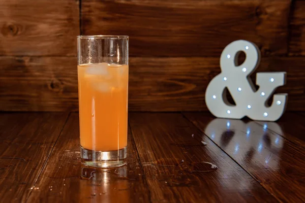 Segelas jus segar yang diperas pada latar belakang kayu dan ampersand yang bersinar — Stok Foto