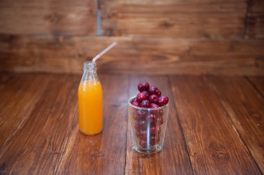 Tatlı kiraz, ahşap zemin üzerinde bir bardakta siyah kiraz ve cam şişede taze sulu