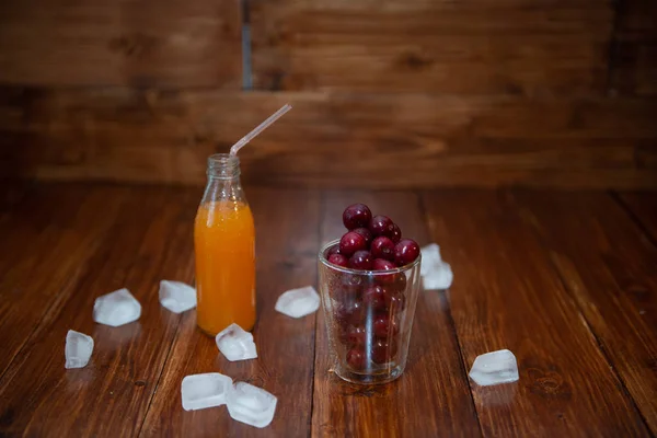 Cereza dulce, cerezas negras en un vaso sobre fondo de madera con fresco jugoso en botella de vidrio — Foto de Stock