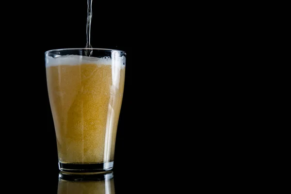 Schiuma di birra versato in un bicchiere su uno sfondo nero con spazio copia — Foto Stock