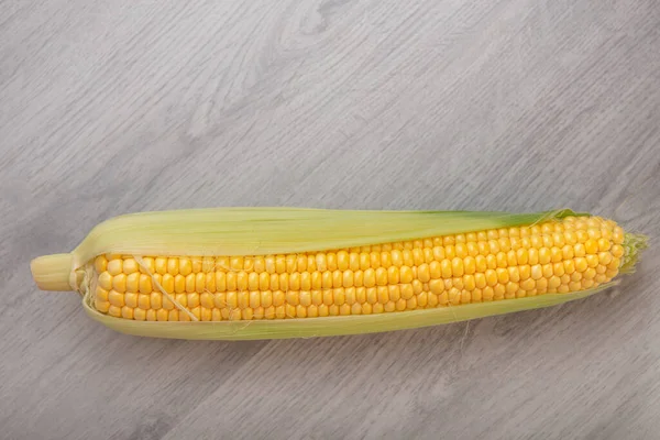 Raw corn cob with husks on a wooden background — Stock Photo, Image