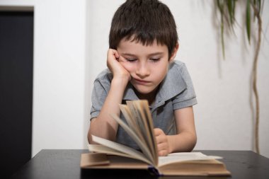 Sıkılmış bir çocuk kitap okuyor.