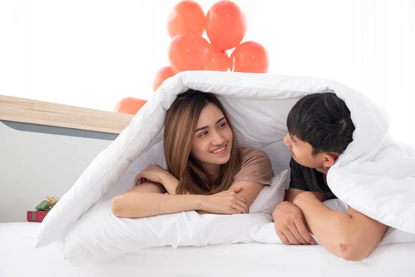 在情人节的早晨 一对快乐的年轻夫妇在卧室里醒来后 在床底下的毛毯下互相交谈 亚洲的年轻夫妇们正享受在一起共度情人节的时光 — 图库照片