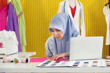 İş sahibi olarak tesettür takan genç ve güzel bir Asyalı Müslüman kadın tasarımcı atölyesinde dikmeye hazırlanan kumaşın boyutunu ölçmeye başlıyor..
