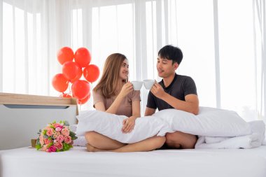 Mutlu genç bir çift yatak odalarında tezahürat yapmak için beyaz bardak kaldırıyor. Kadeh kaldırıyorum..