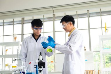 Bilim, Kimya, Teknoloji, Biyoloji ve Laboratuar Konsepti - Asyalı kıdemli ve kıdemsiz bilim adamlarının portresi deney bardağı şişesinde deneysel sonuçlarını gösteriyor.