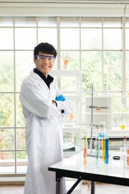 Bilim, Kimya, Teknoloji, Biyoloji ve Laboratuar Konsepti - gülümseyen Asyalı genç bilim adamı portresi teçhizatla dolu laboratuvar masasının önünde duruyor.