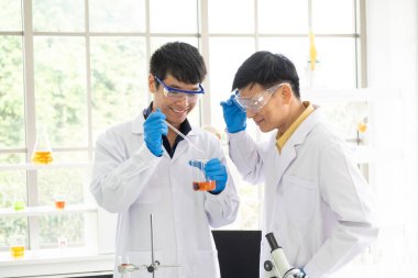 Bilim, Kimya, Teknoloji, Biyoloji ve Laboratuar Konsepti - Asyalı kıdemli bilim adamı, Asyalı kıdemsiz bilim adamının cam deney tüpü ile sonuçlanacağını düşünüyor.