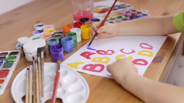 Το παιδί γράφει γράμματα με ένα πινέλο σε ένα λευκό φύλλο χαρτί — Αρχείο Βίντεο
