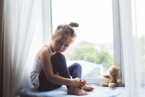 Sad girl sitting on a window sill