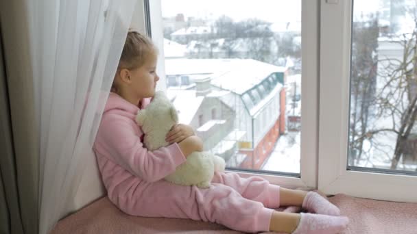 Маленькая грустная девочка смотрит в окно — стоковое видео