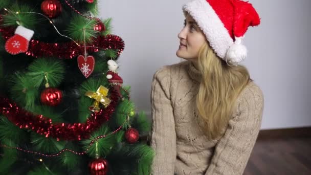 Flicka i Santas cap sitter vid nyår trädet och drömmar — Stockvideo