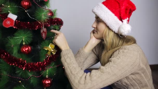 Flickan sitter vid julgranen och tänker — Stockvideo