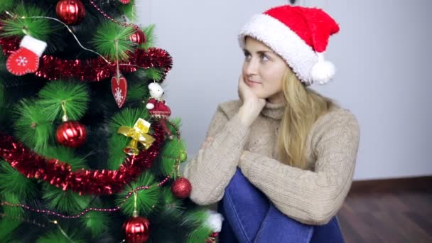 Kvinna sitter vid julgranen och tycker — Stockvideo
