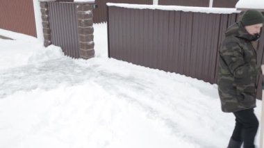 Adam kar evin yanında büyük bir kürekle temizler.