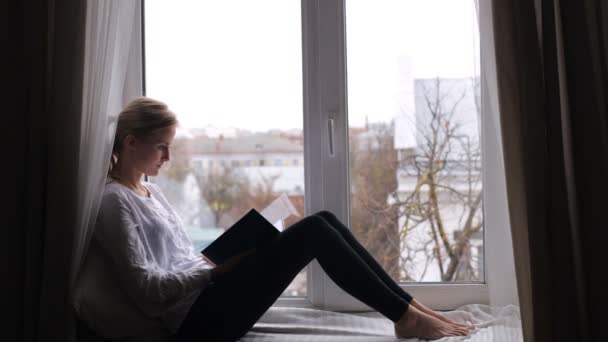 Girl sits on the windowsill and reads — Stock Video